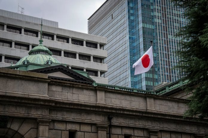 Ibu pejabat Bank of Japan di Tokyo dengan bendera Jepun berkibar dan menara pejabat kaca moden di belakang