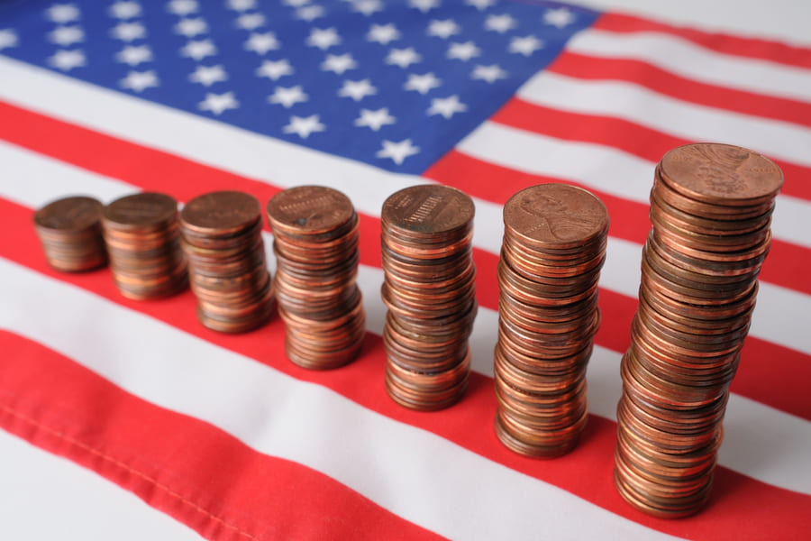 Stacks of US penny coins rising in height from left to right on an American flag, symbolising US inflation and economic growth
